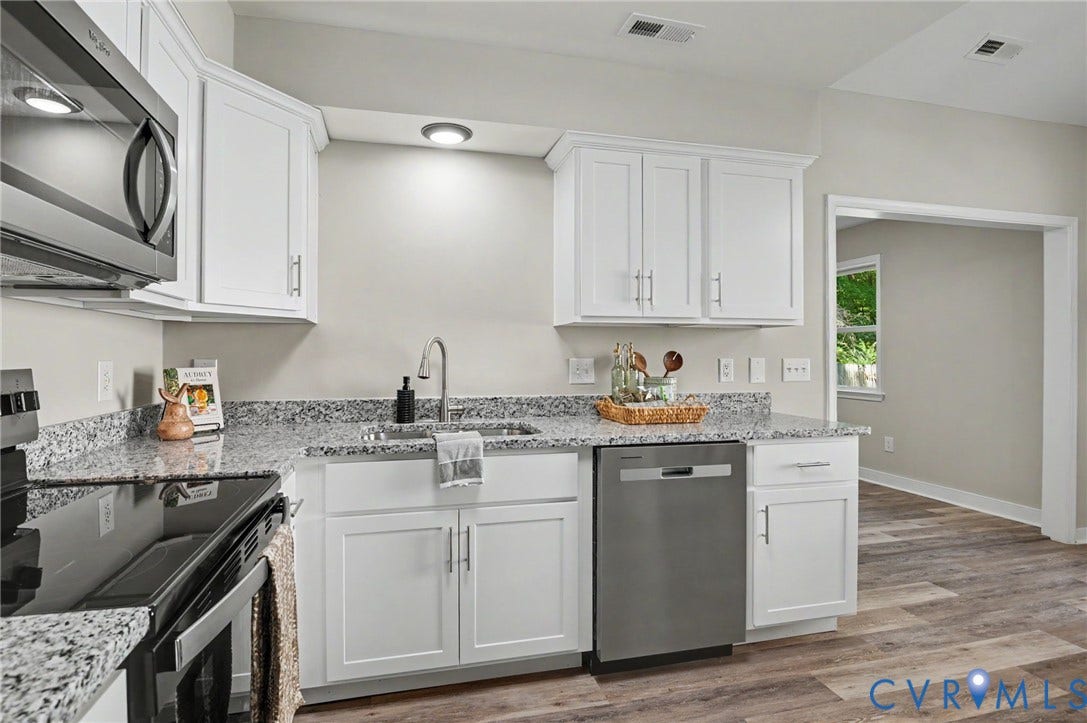 White cabinetry with brushed nickel hardware, speckled countertops, stainless steel appliances, and wood-finish flooring