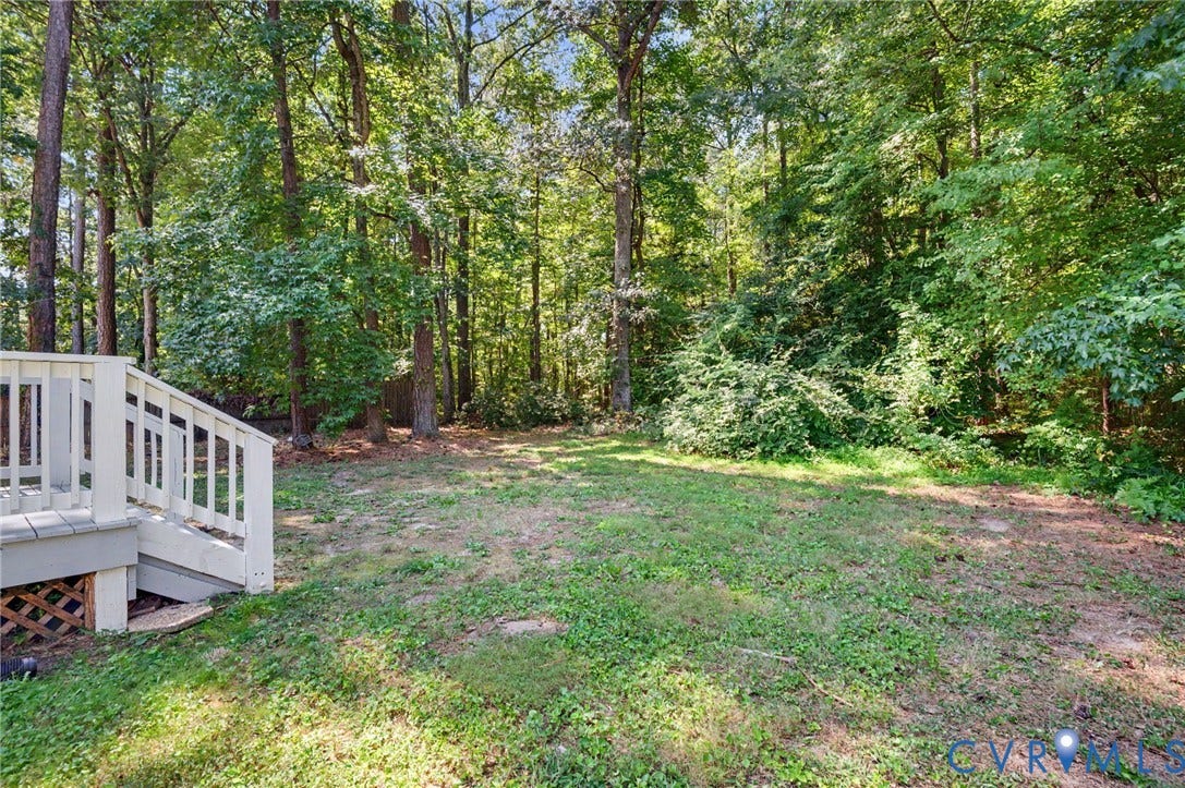 Expansive backyard featuring a natural treeline, mature trees, and a multi-level deck with white railings