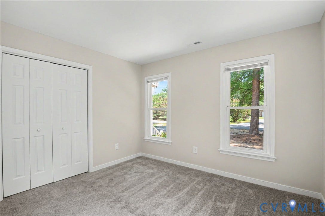Light-colored walls, grey carpet flooring, two double-hung windows, and a bi-fold closet door