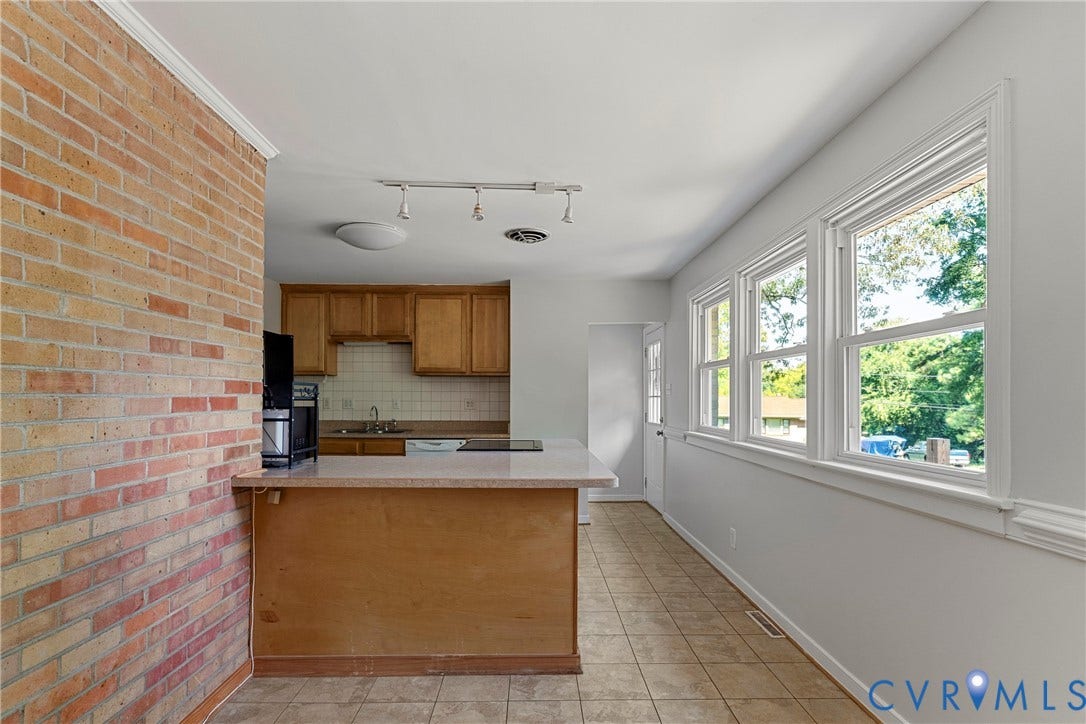 5968 Forest Hill Avenue, Westlake Hills, Richmond, VA 23225 Brick accent wall, L-shaped kitchen counter, light wood-finish cabinetry, tile flooring, and a wall of windows