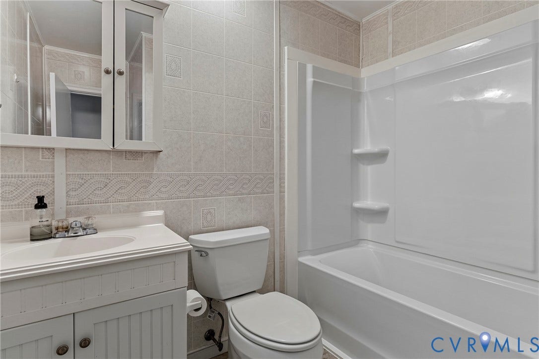 5968 Forest Hill Avenue, Westlake Hills, Richmond, VA 23225 Bathroom featuring a white vanity with beadboard paneling, mirrored medicine cabinet, white porcelain toilet, and a white fiberglass tub with an integrated shower surround