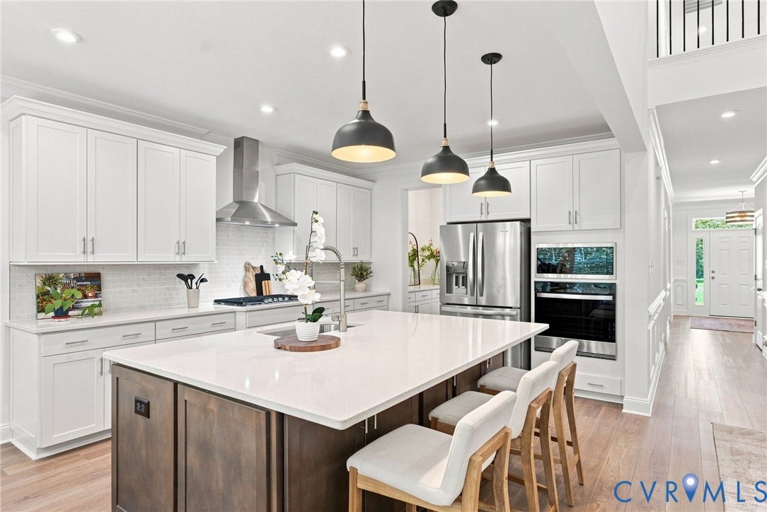 White cabinetry with crown molding, stainless steel appliances, a large center island with counter seating, light wood-finish flooring, and pendant lighting