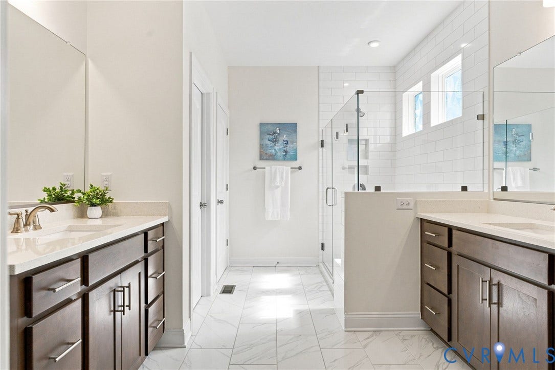 Dual vanity sinks with stone countertops, dark wood cabinetry, a glass-enclosed shower, subway tile shower surround, and tiled flooring