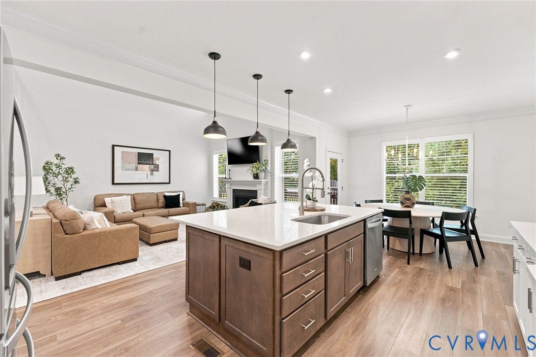 Open-concept living space featuring wood-finish flooring, a kitchen island with integrated sink, recessed lighting, and a fireplace with a mantel