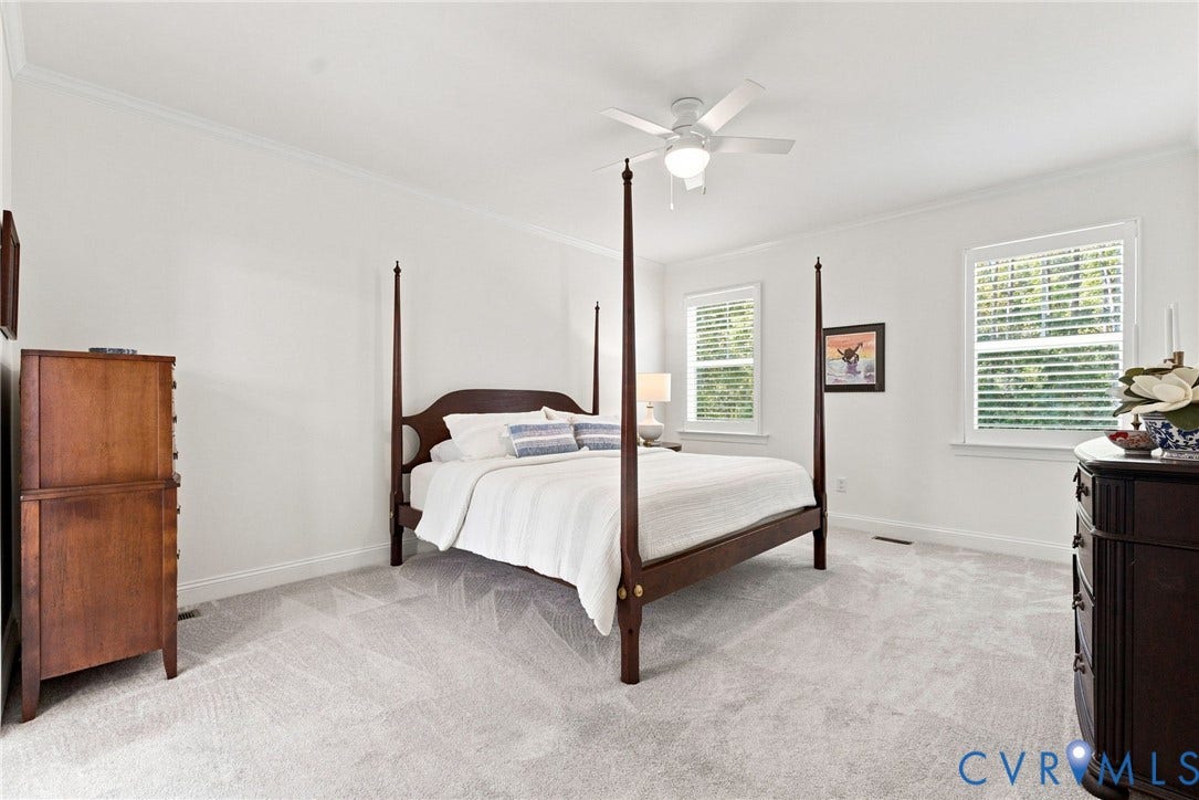 Light-colored wall-to-wall carpeting, white walls, two windows with blinds, and a ceiling fan with light fixture