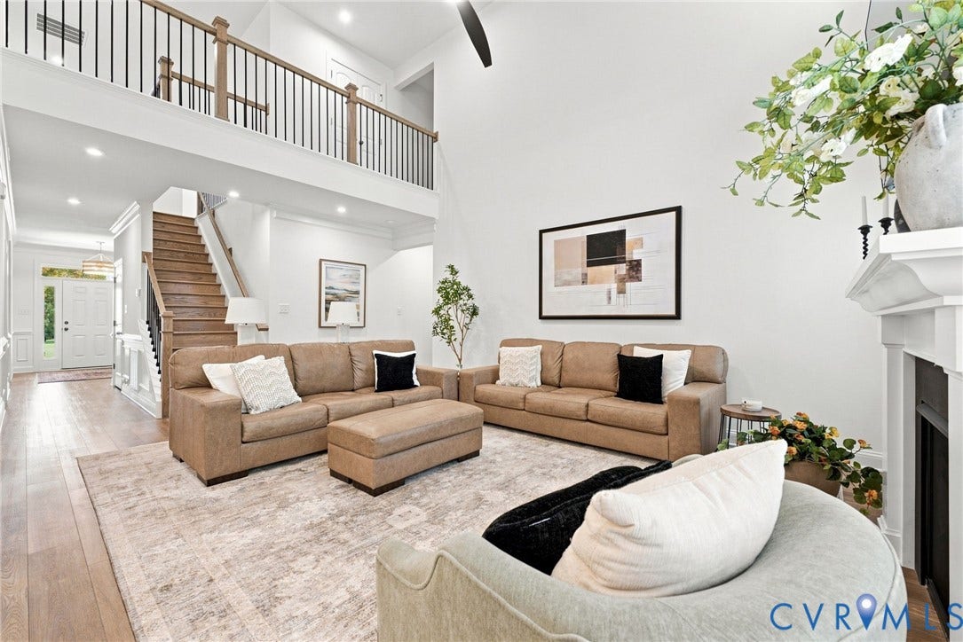 Two-story living area with high ceilings, wood-finish flooring, a fireplace with a white mantel, and a prominent staircase with wood and metal railings