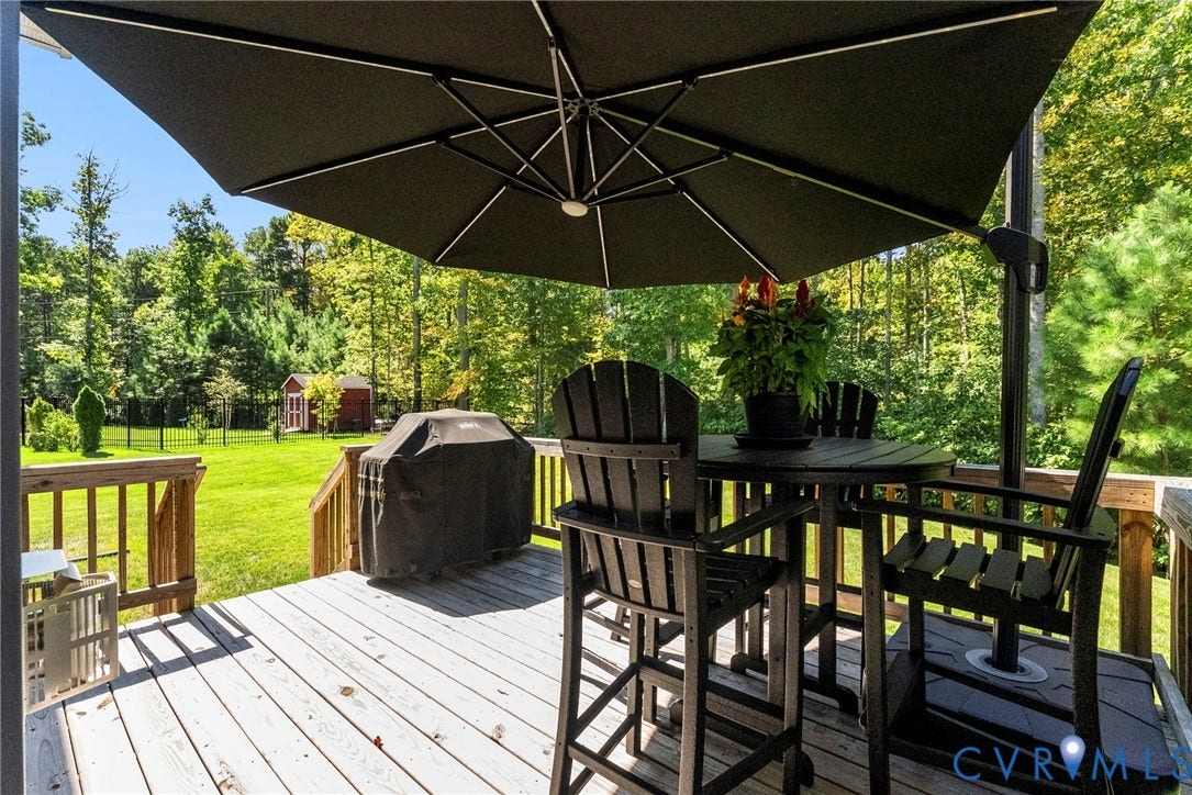Expansive wood deck with wood railings, overlooking a large grassy yard with mature trees