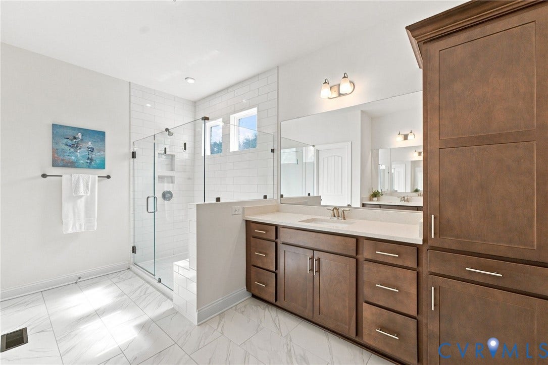 Spacious bathroom featuring a glass-enclosed shower with subway tile, dual vanity with wood cabinetry, and a built-in storage cabinet