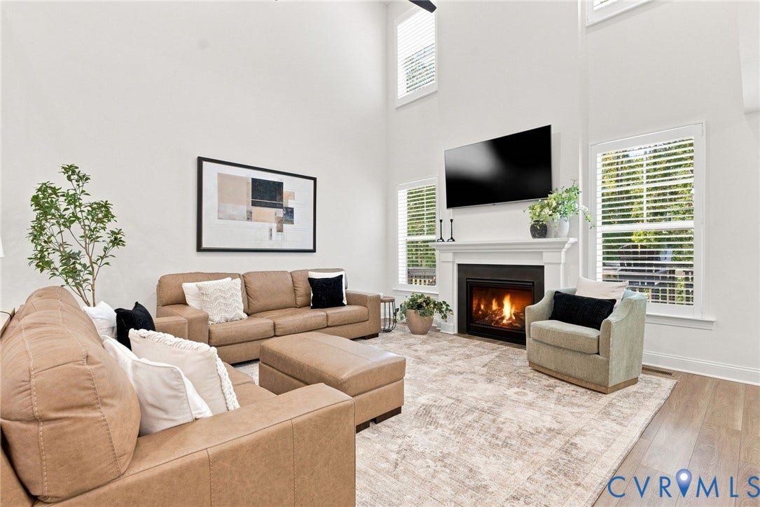 Vaulted ceilings, wood-finish flooring, white mantle fireplace, and multiple windows with horizontal blinds