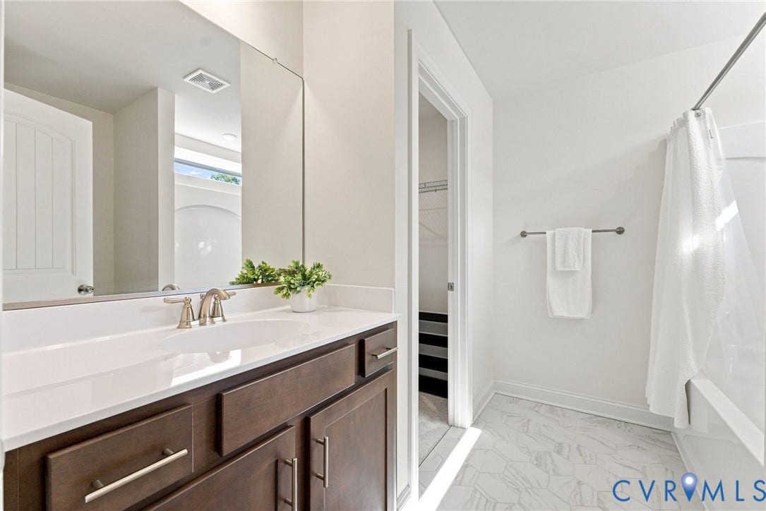 White countertop with an undermount sink, wood-finish cabinetry, and a full-width mirror