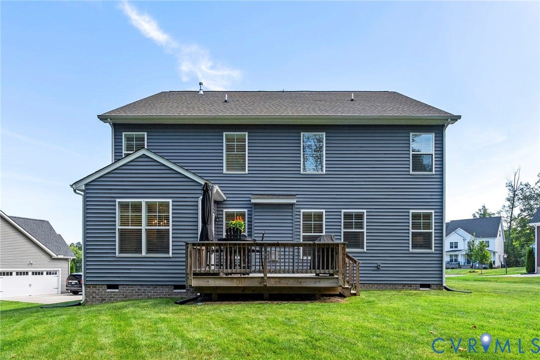Expansive green lawn, multi-level wood deck, blue horizontal siding, and multiple windows