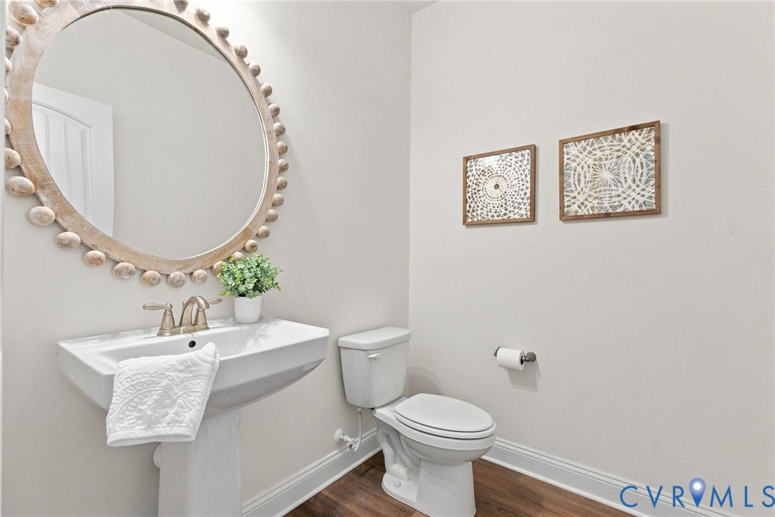 Pedestal sink with a two-handle faucet, round wall-mounted mirror, and wood-finish flooring