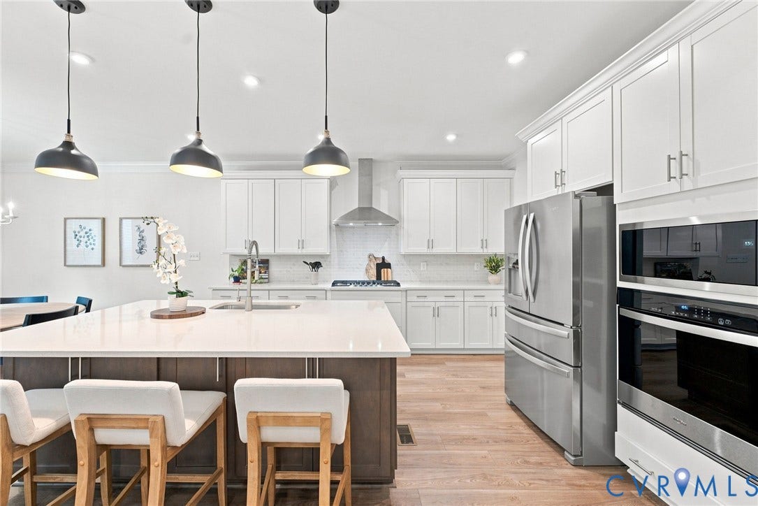 Contemporary kitchen featuring a large island with a light-toned countertop, white cabinetry with silver hardware, stainless steel appliances, and wood-finish flooring