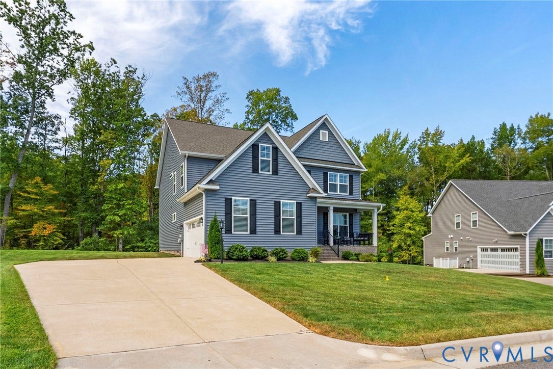 Blue siding exterior with white trim, a covered front porch, an attached two-car garage, a concrete driveway, and a manicured lawn