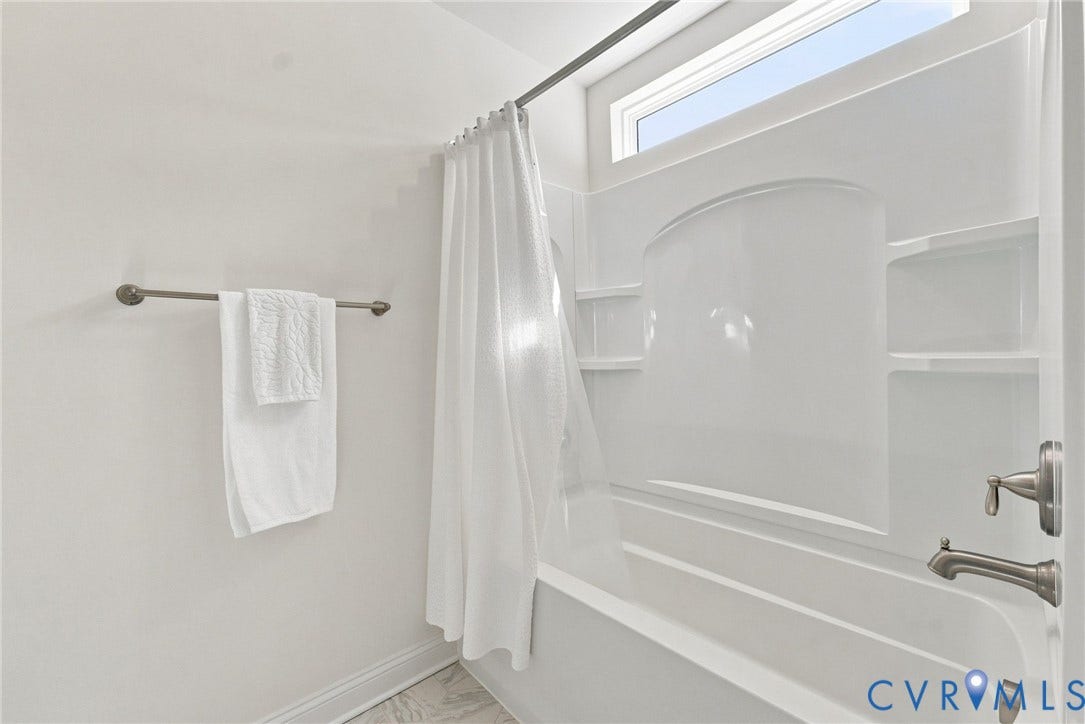 White tub and shower combination with brushed nickel fixtures and an upper transom window