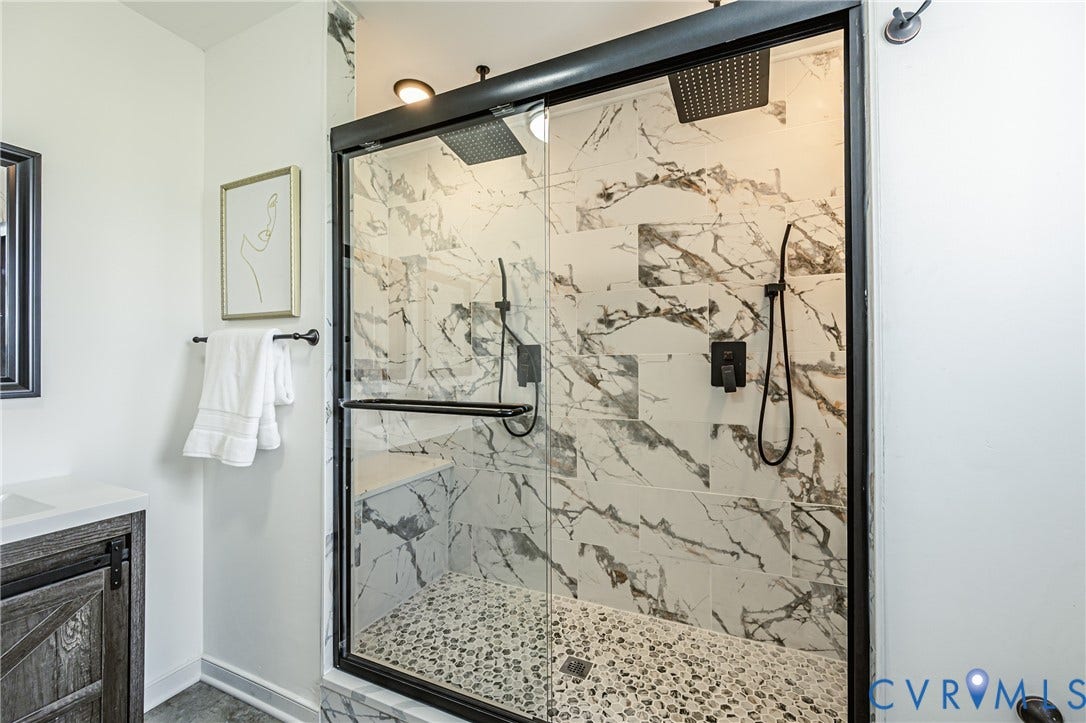 4008 River Road, Chesterfield, VA 23803 Glass-enclosed shower with a black frame, featuring a built-in bench, marble-finish wall tiling, and a pebble-finish shower floor
