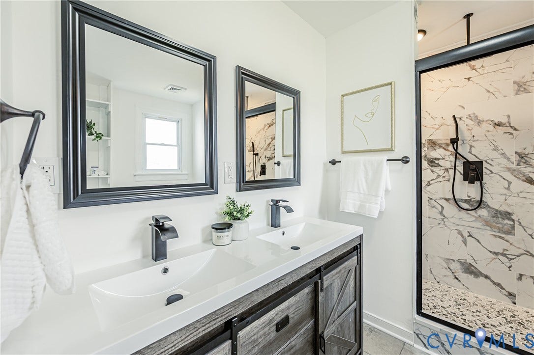 4008 River Road, Chesterfield, VA 23803 Dual basin vanity with wood-finish cabinetry, black framed mirrors, matte black fixtures, and a glass-enclosed shower with marble-look tile