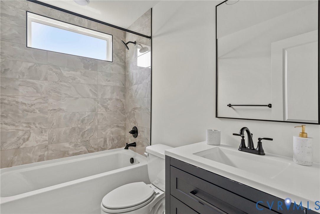 2004 Newbourne Street, Richmond, VA 23223 Bathroom featuring a built-in tub with a shower, a sleek vanity with a rectangular sink, a black-framed mirror, and a horizontal window