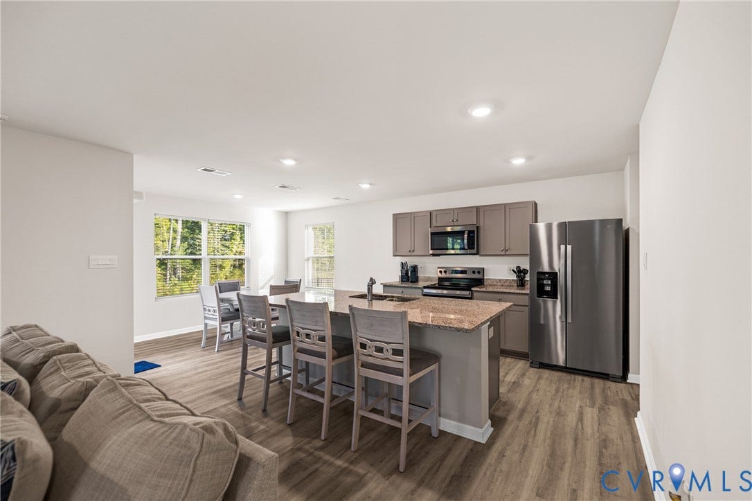 7974 Arbor Marsh Terrace, New Kent, VA 23124 Open-concept living space featuring wood-finish flooring, recessed lighting, a kitchen island with seating, stainless steel appliances, and ample natural light from multiple windows