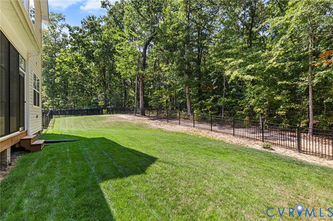 Expansive grassy yard with a black metal fence and mature trees