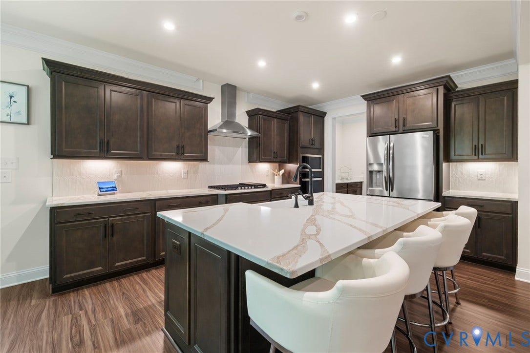 Kitchen featuring dark wood cabinetry, white countertops, stainless steel appliances, a center island with seating, and wood-finish flooring
