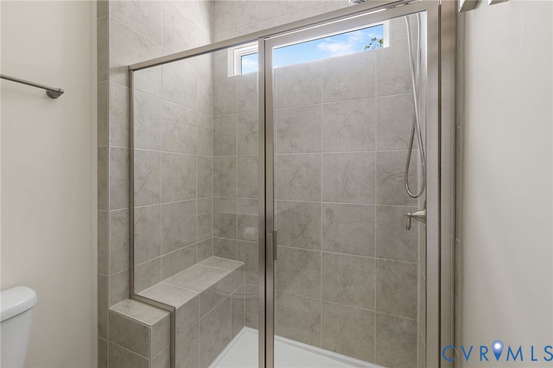 Walk-in shower with full-height tile surround, glass enclosure, built-in bench, and an upper transom window