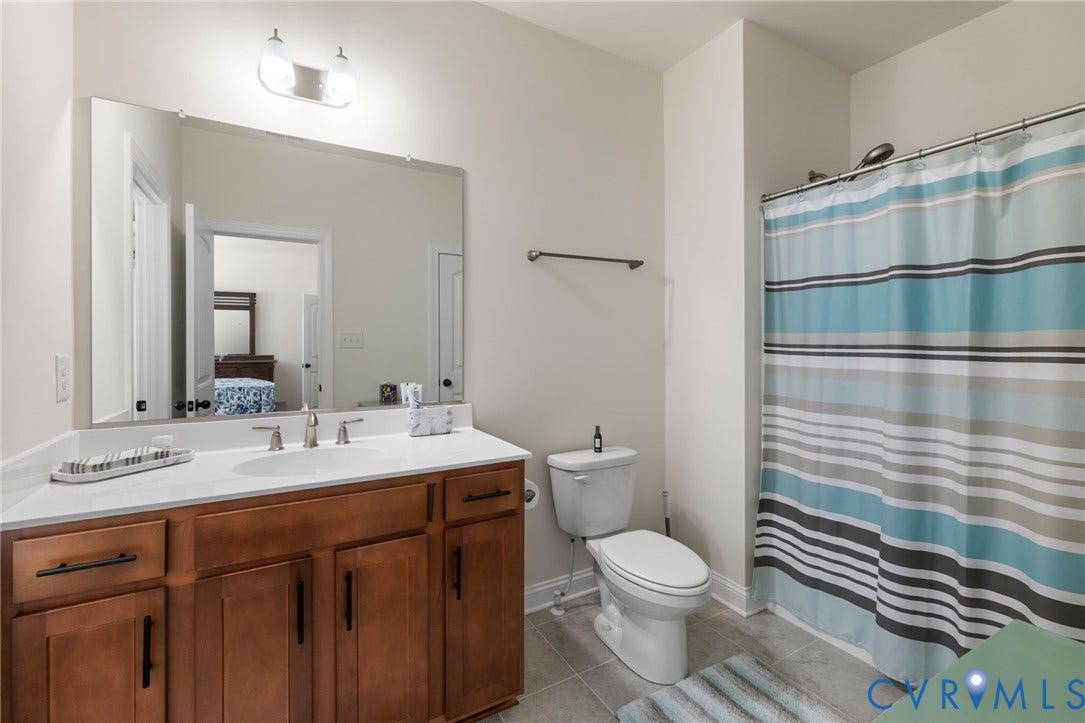 Wood-finish vanity with an integrated sink, brushed nickel faucet, large wall-mounted mirror, and a built-in shower