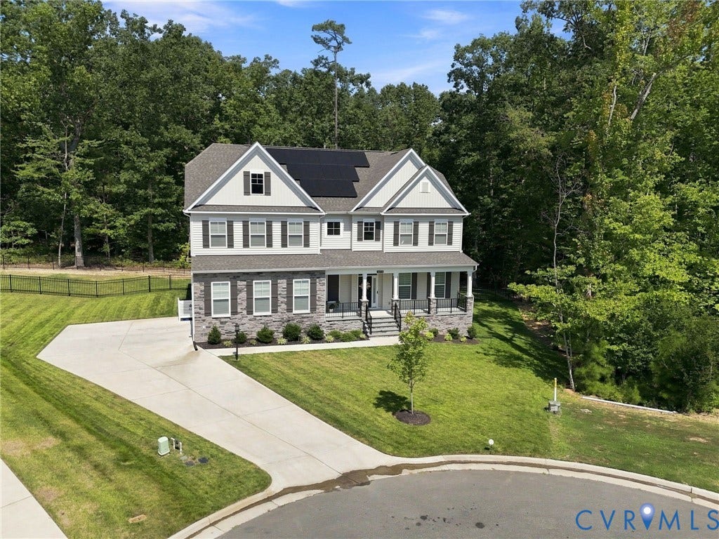 Two-story residence featuring a stone and siding facade, a covered front porch, an asphalt shingle roof with solar panels, and a concrete driveway