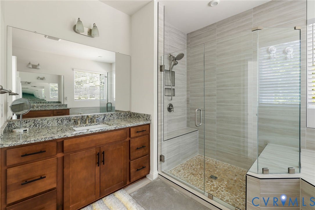 Spacious bathroom featuring a large vanity with an integrated sink, a generous mirror, and a walk-in shower with a built-in bench