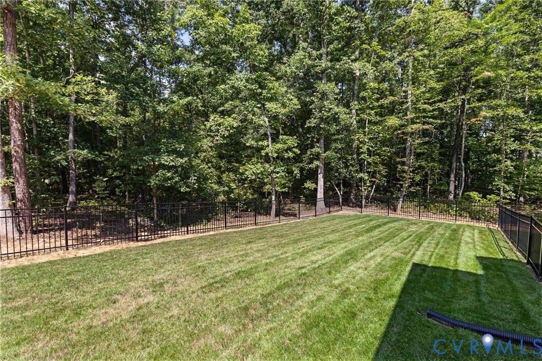 Expansive grass lawn with a black metal fence bordering a dense wooded area