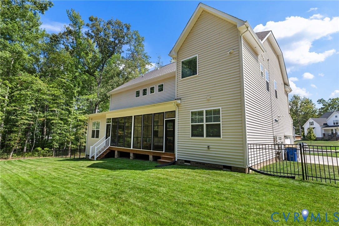 Expansive green lawn with a screened-in porch and white railing, featuring exterior siding and a black metal fence