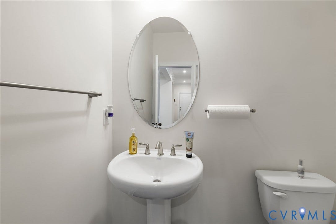 Pedestal sink with a polished chrome faucet, oval wall-mounted mirror, and white toilet