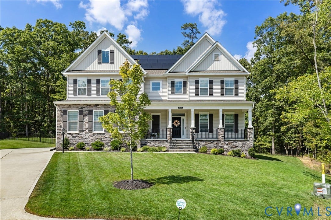 Two-story residence featuring light-toned siding, dark window shutters, stone accents, and a covered front porch with pillars