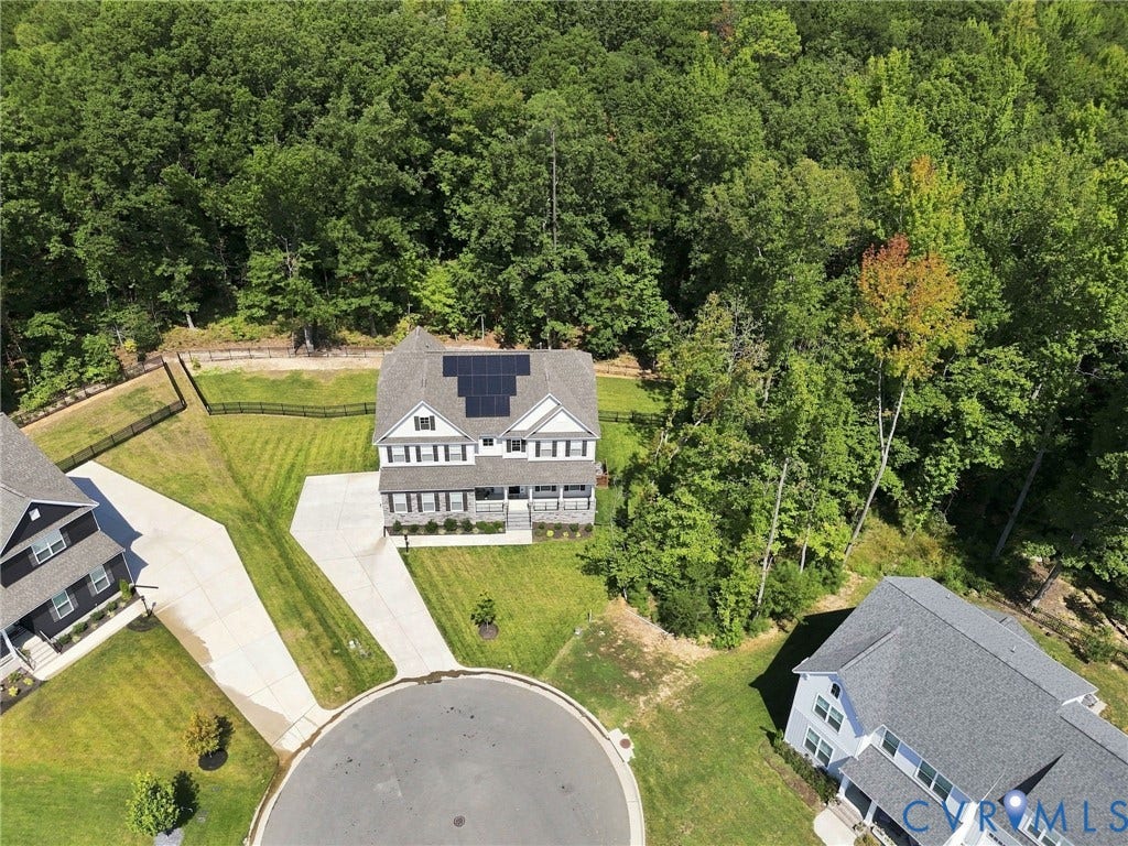 Property featuring a two-story exterior, multiple solar panels, a concrete driveway, an expansive lawn, and mature trees