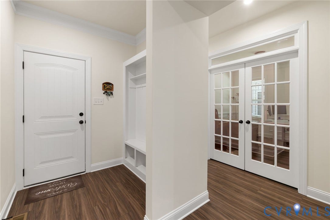 Wood-finish flooring throughout, white interior door, custom built-in storage bench, and white French doors with transom