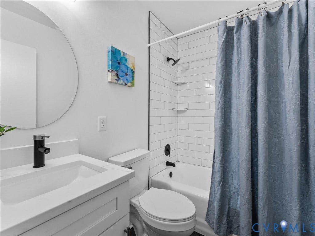 3626 Reynolds Road, Richmond, VA 23223 Full bathroom featuring a vanity with an integrated sink and matte black faucet, a circular wall mirror, and a tiled shower/tub combination with built-in shelving