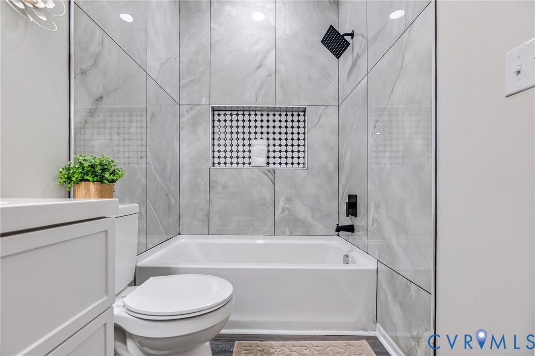 Bathtub with tiled surround, black fixtures, and a recessed tile niche