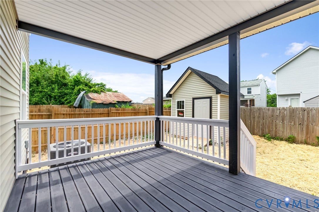 Covered outdoor deck with white railing, dark wood-finish flooring, and a shed with white siding and black trim