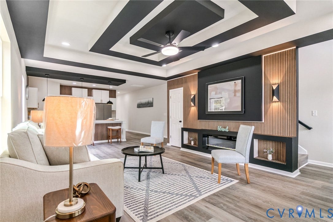 Tray ceiling with recessed lighting and ceiling fan, wood-finish flooring, built-in entertainment console with display shelves, accent wall with vertical wood paneling, and dual pendant lights