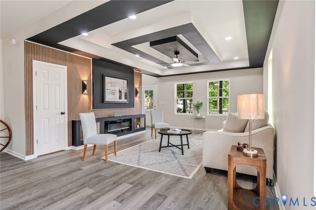 Expansive living area with wood-finish flooring, a multi-tiered tray ceiling with recessed lighting, and large windows