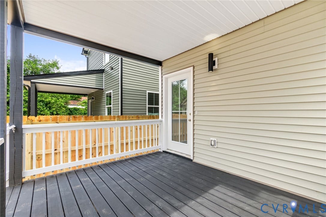 Covered outdoor deck with dark wood-finish flooring, white railing, and a glass-paneled door