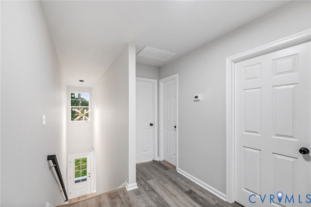 Wood-finish flooring throughout, white paneled doors, and a staircase with a black handrail