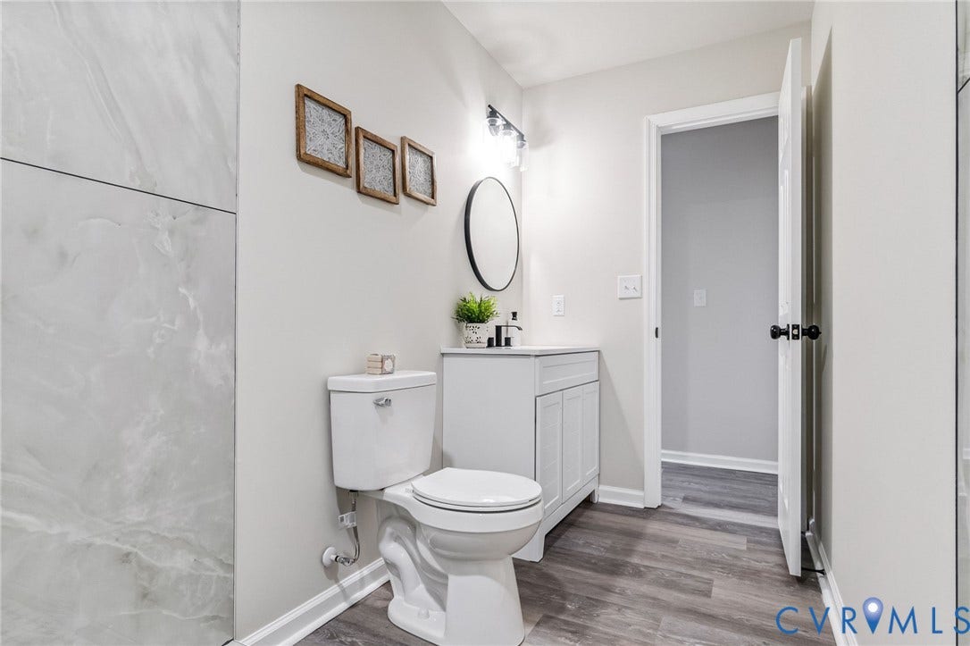 White vanity with a vessel sink, dark wood-finish flooring, and a round wall-mounted mirror