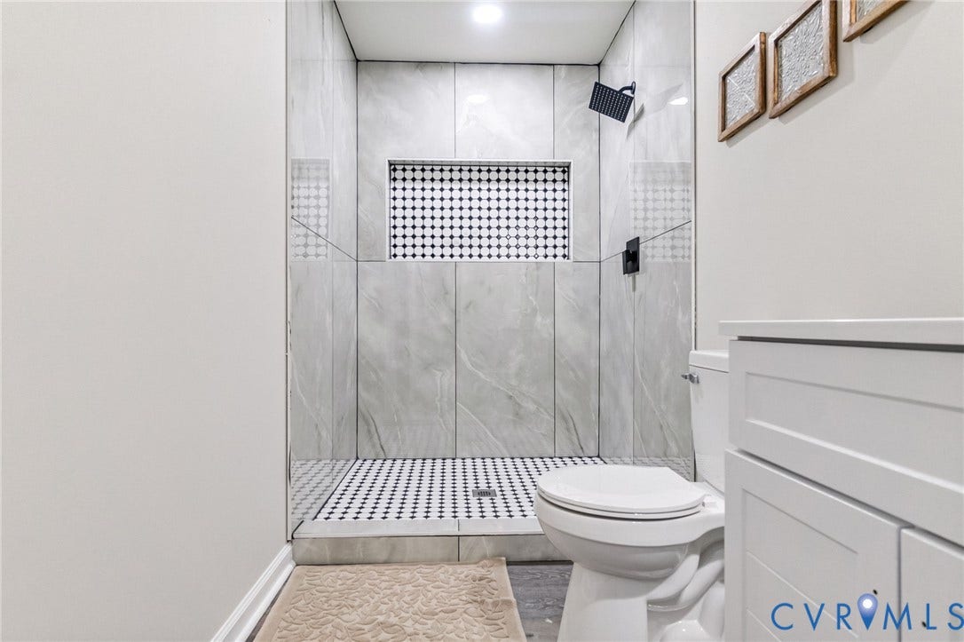 Walk-in shower with large format tile surround, black and white mosaic tile flooring, built-in shower niche, and matte black fixtures