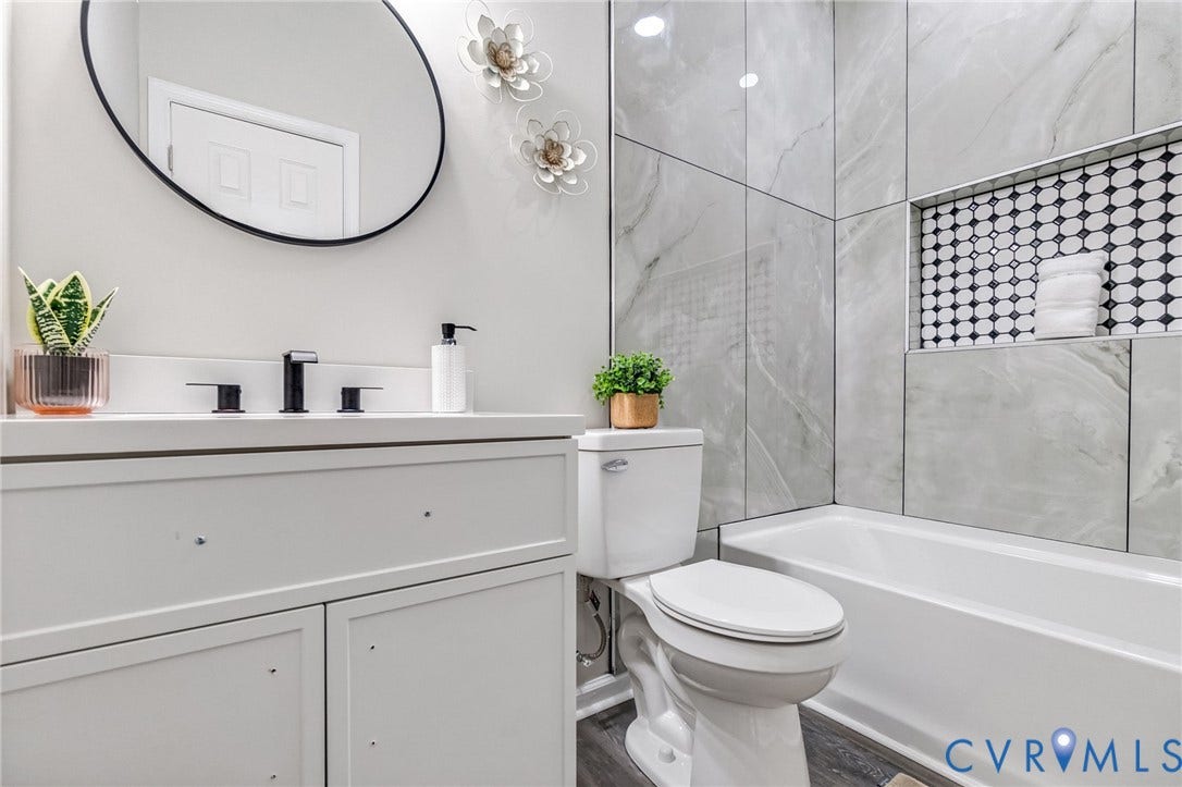 White vanity with black hardware, white rectangular sink, light gray wall tile, white bathtub, and wood-finish flooring