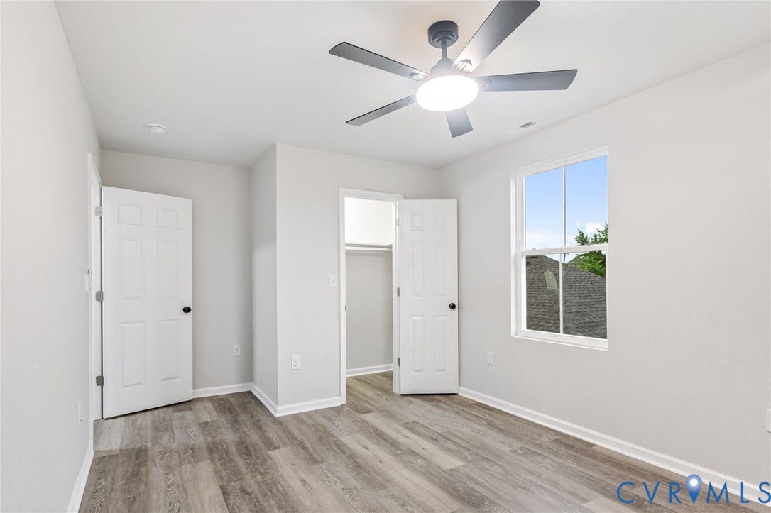 Wood-finish flooring, light gray walls, white trim, ceiling fan with integrated lighting, and a double-hung window