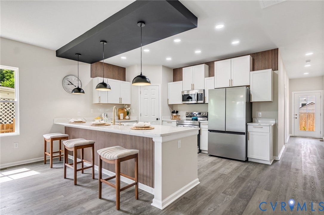 Modern kitchen featuring white cabinetry, stainless steel appliances, a breakfast bar island with a light-toned countertop, and wood-finish flooring