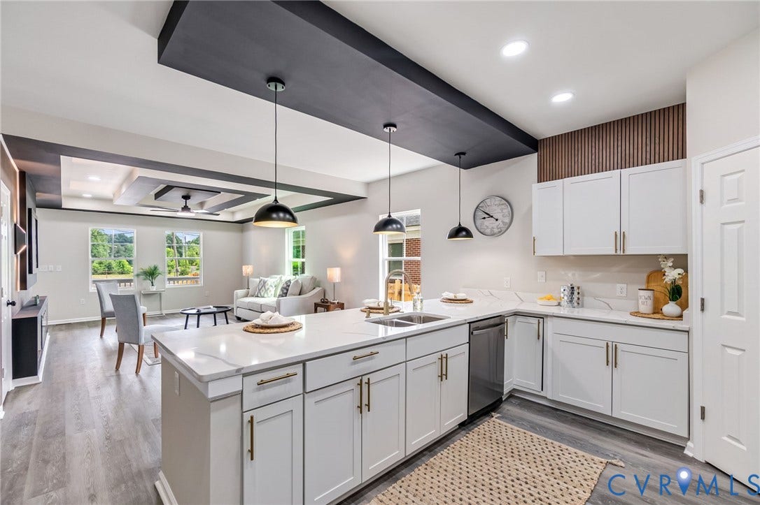 Open-concept layout featuring a kitchen island with stone countertops, white cabinetry with gold-tone hardware, wood-finish flooring, and a tray ceiling detail