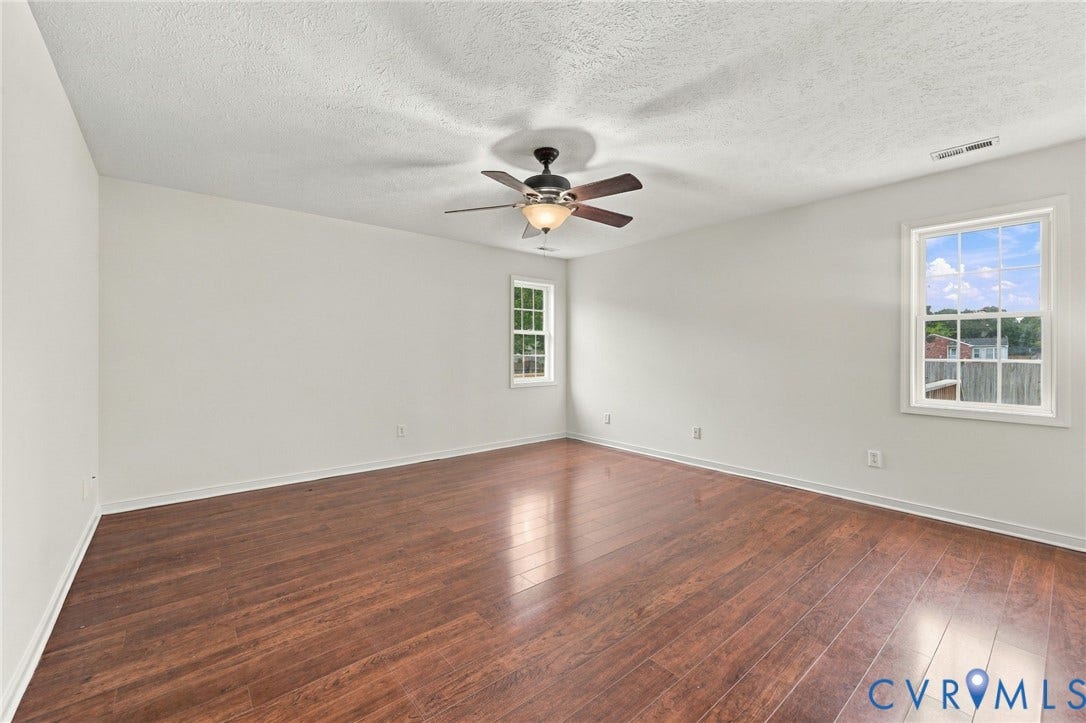 Spacious room featuring wood-finish flooring, white painted walls, two windows, and a ceiling fan with integrated lighting