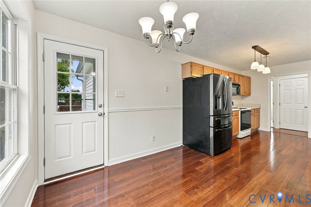Wood-finish flooring throughout, white paneled door with glass inserts, modern ceiling light fixture, kitchen with wood cabinetry, and a black French door refrigerator